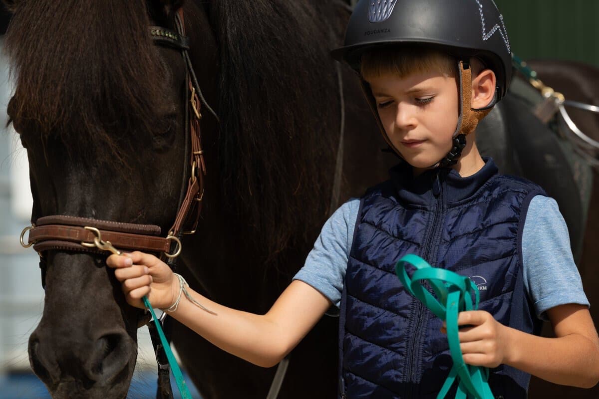 Ein Junge mit Reithelm führt sein dunkles Pony am Strick