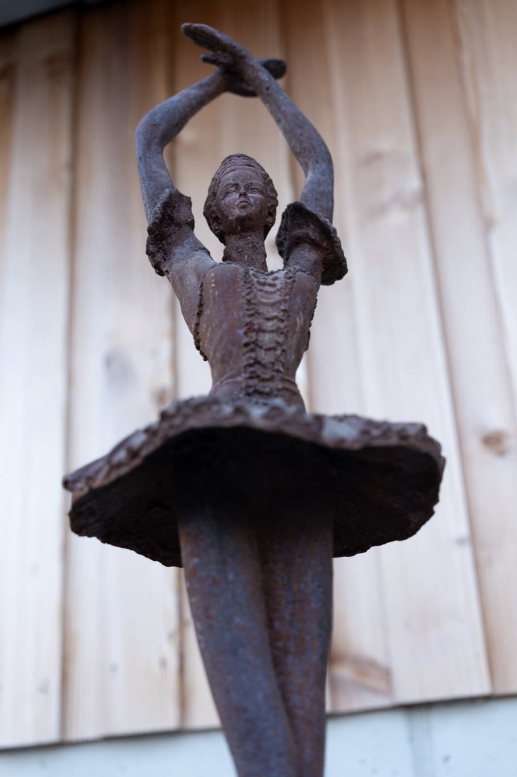 Eiserne Skulptur einer Tänzerin mit erhobenen Armen vor der hellen Holzwand des Stalls